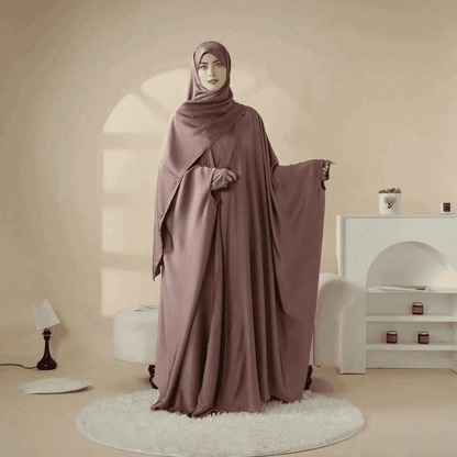 Woman wearing 5 piece satin abaya set in mauve color by Fabaya UK standing in stylish room