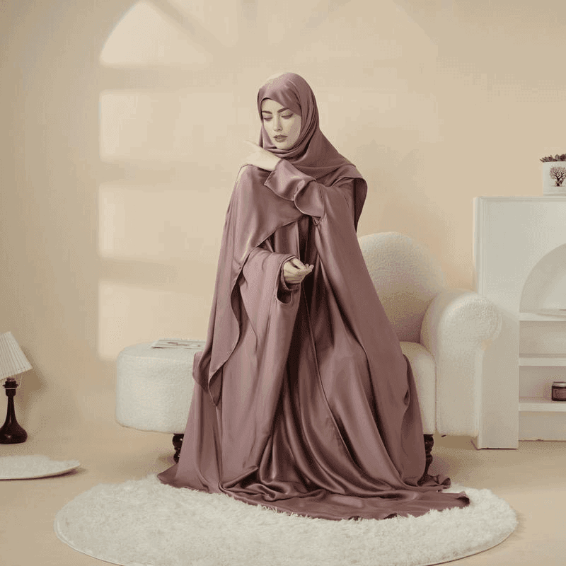 Woman wearing a mauve 5 piece satin abaya set sitting gracefully on a white rug in a cozy beige room