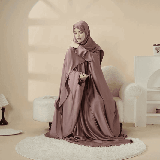 Woman wearing a mauve 5 piece satin abaya set sitting gracefully on a white rug in a cozy beige room