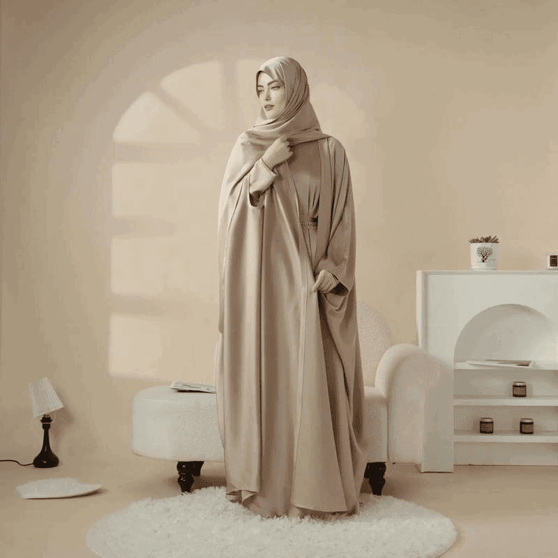 Woman wearing a beige 5 piece satin abaya set by Fabaya UK standing in a stylish neutral-toned room