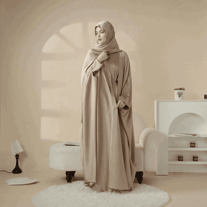 Woman wearing a beige 5 piece satin abaya set by Fabaya UK standing in a stylish neutral-toned room