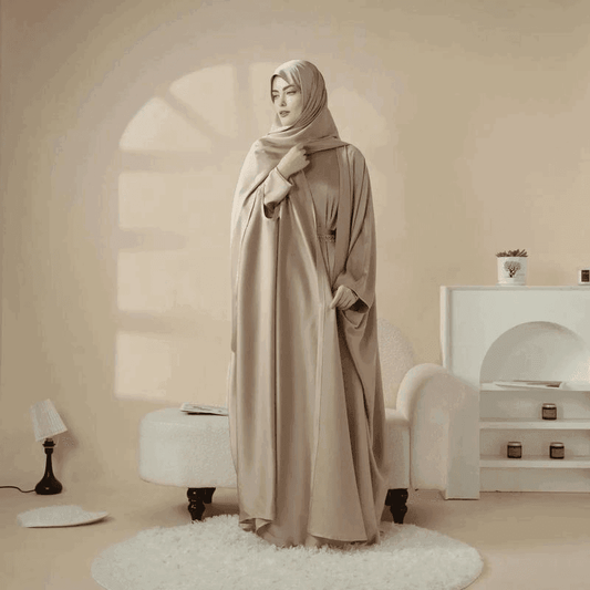 Woman wearing a beige 5 piece satin abaya set by Fabaya UK standing in a stylish neutral-toned room