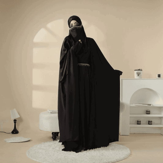 Woman wearing a black 5 piece satin abaya set by Fabaya UK in a minimalist beige room