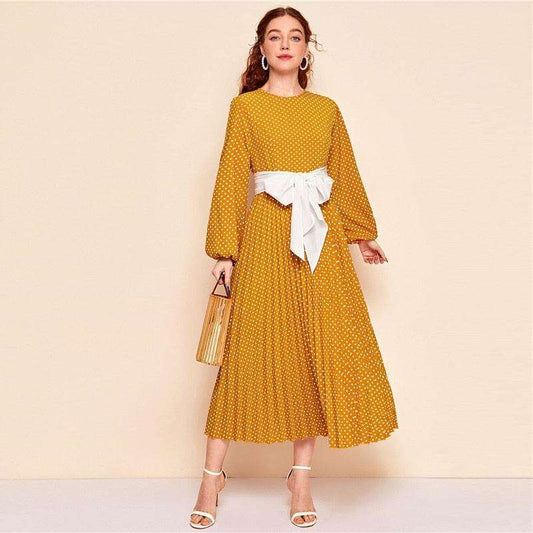 Woman wearing mustard yellow dress with white polka dots and white waist bow holding a handbag