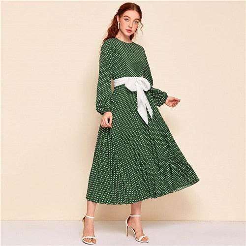 Woman wearing a green polka dot abaya dress with long sleeves and a white waist bow belt