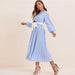 Woman wearing a blue polka dot abaya dress with long sleeves and a white waist tie belt