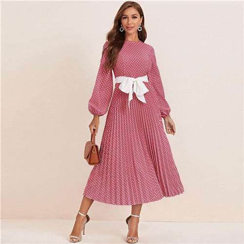 Woman wearing a pink polka dot abaya dress with a white bow belt and long sleeves