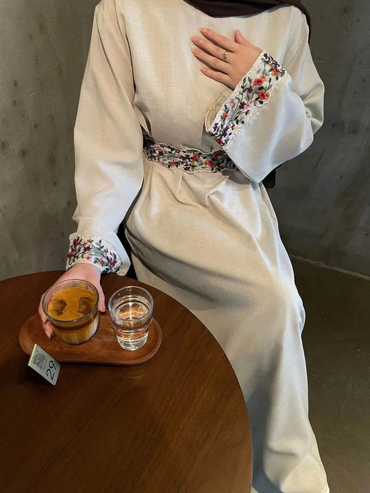 Fabaya UK cotton linen modest dress with floral trim on cuffs and waist sitting at wooden table