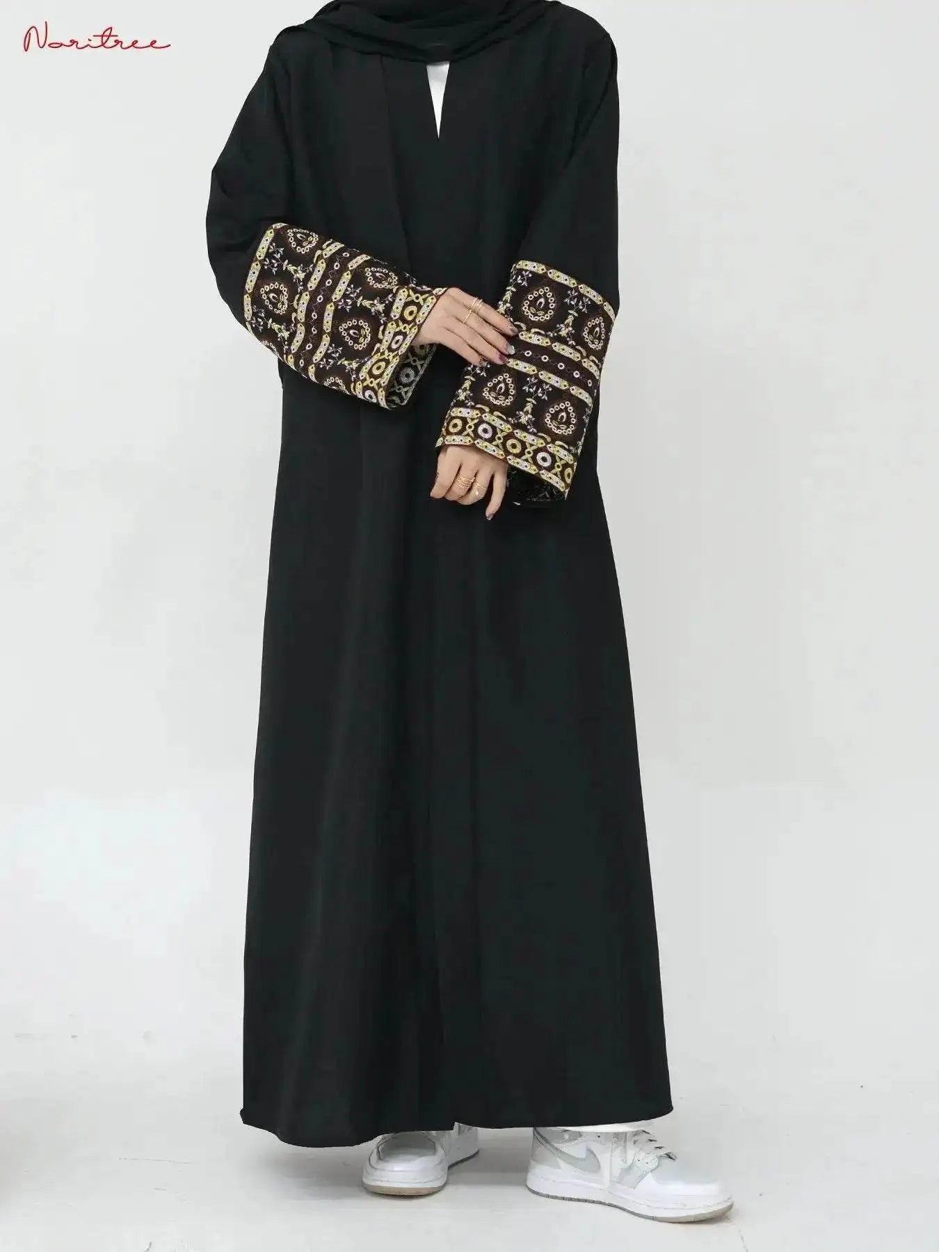 Black embroidered abaya kimono with intricate gold and brown sleeve designs paired with white sneakers