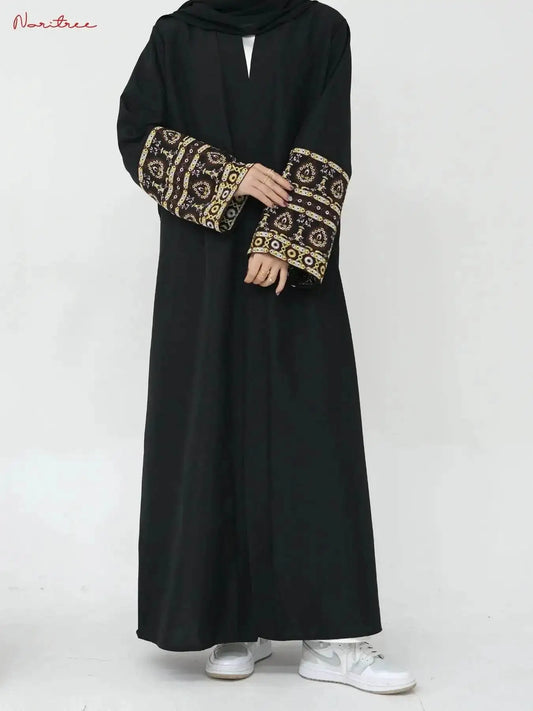Black embroidered abaya kimono with intricate gold and brown sleeve designs paired with white sneakers