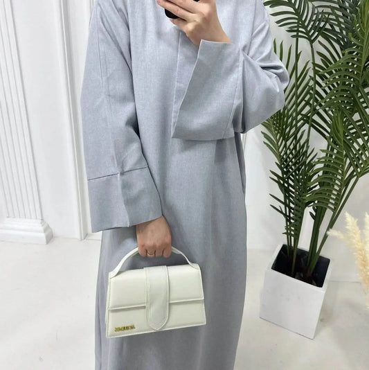 Fabaya UK luxury linen abaya in light gray fabric with wide sleeves and white handbag