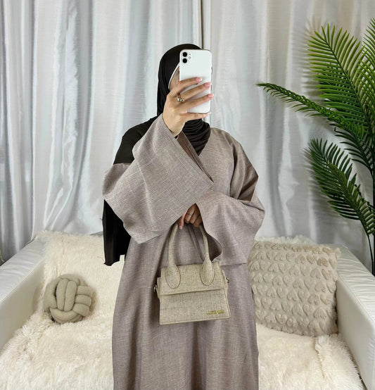 Woman wearing a luxury linen abaya by Fabaya UK holding a matching textured handbag indoors