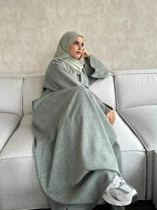 Woman wearing a Fabaya UK luxury linen abaya in light gray sitting on a modern sofa