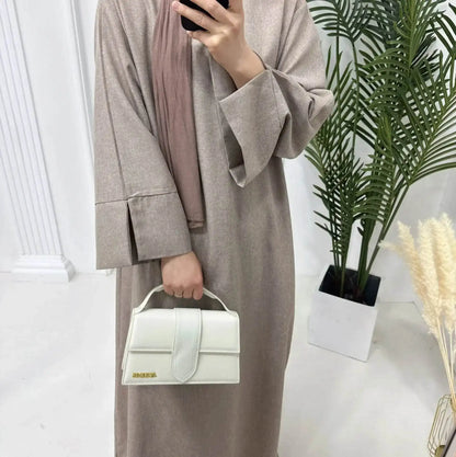 Fabaya UK luxury linen abaya in beige with wide sleeves, styled with a white handbag and brown scarf