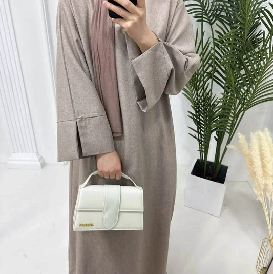 Fabaya UK luxury linen abaya in beige with wide sleeves, styled with a white handbag and brown scarf