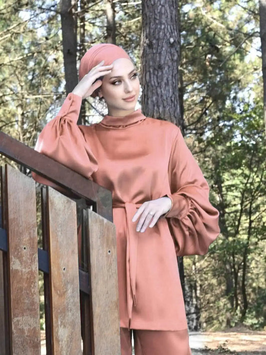 Woman wearing a shiny silky abaya set in soft peach with puffed sleeves and a matching headscarf outdoors
