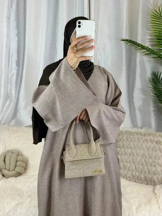 Woman wearing luxury cotton linen abaya dress in beige with wide sleeves holding matching handbag