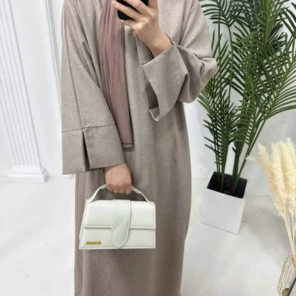 Woman wearing a luxury cotton linen abaya dress in beige holding a white handbag indoors