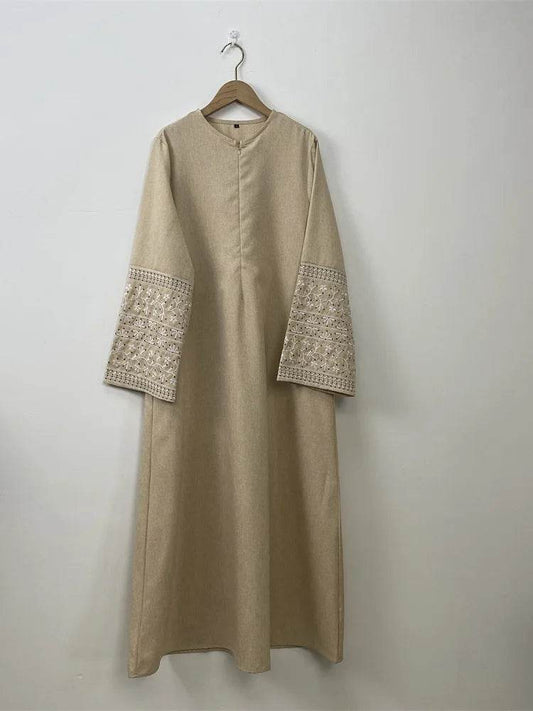 Beige stylish muslim abaya for women with detailed embroidery on wide sleeves hanging on wooden hanger